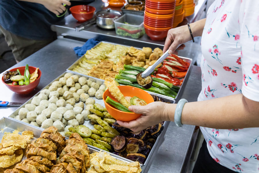 Una persona tomando ingredientes frescos con pinzas en un puesto de comida en China