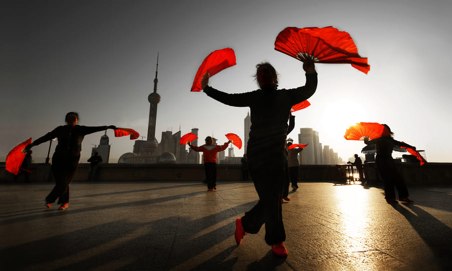 Personas bailando con abanicos rojos en el Bund de Shanghái